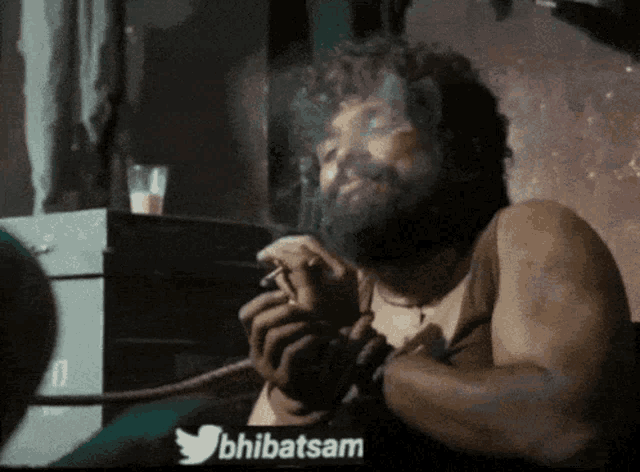 a man with a beard is smoking a cigarette in a dark room with a twitter logo above him