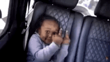 a baby is sitting in a car seat and giving the middle finger .