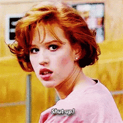a woman with red hair is wearing a pink shirt and says `` shut up '' .