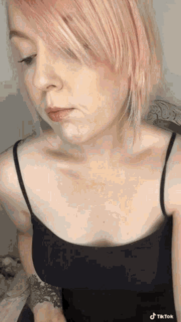 the woman is wearing a black tank top and has pink hair .