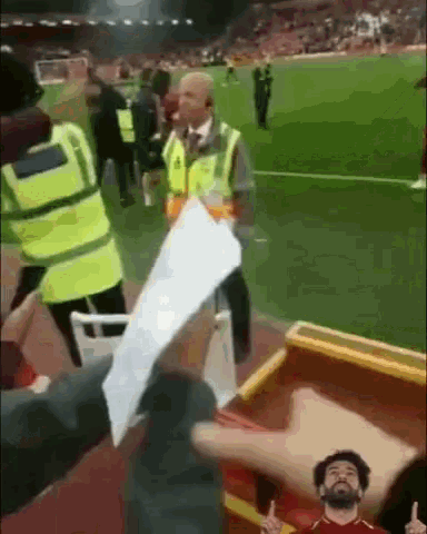 a man in a yellow vest is holding a piece of paper on a soccer field