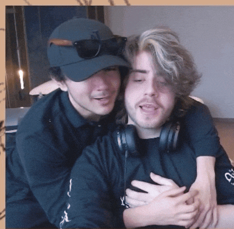 a man wearing headphones is hugging another man wearing a hat
