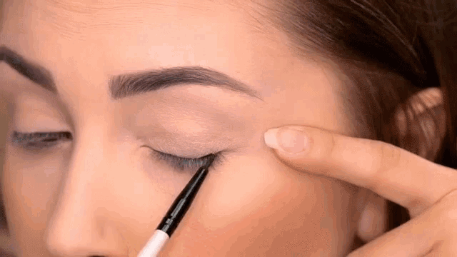 a woman is applying eyeliner with a brush to her eye .