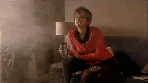 a woman sitting on a couch smoking a cigarette and holding a can