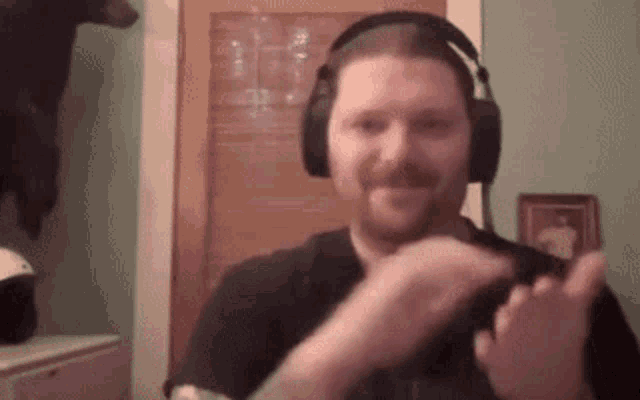 a man wearing headphones is clapping his hands in front of a bear .