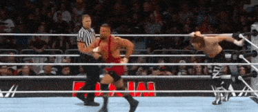 two men are wrestling in a wrestling ring with a referee in the background .