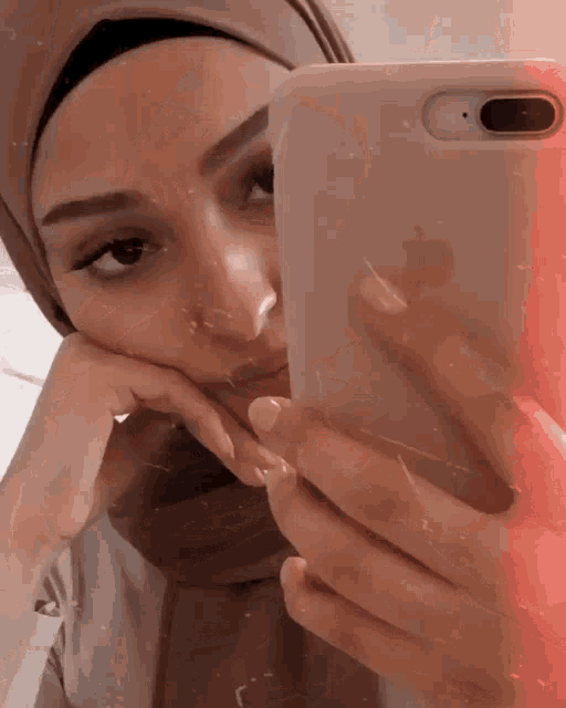 a woman wearing a hijab takes a selfie with her iphone