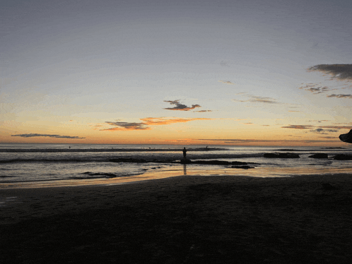 a person stands on a beach at sunset looking out over the ocean