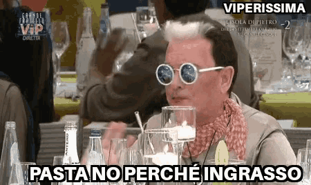 a man wearing sunglasses is sitting at a table with wine glasses and says " viperissima "