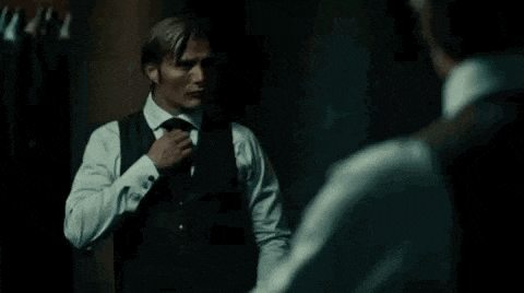 a man in a white shirt and tie is standing in front of a mirror .