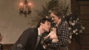 a man kisses a woman on the cheek while she holds a small dog