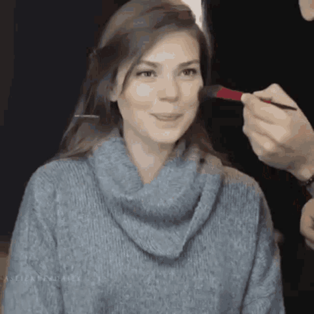 a woman in a blue sweater is getting her makeup applied