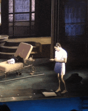 a man in a white shirt is standing on a stage in front of a chair with the letter j on it