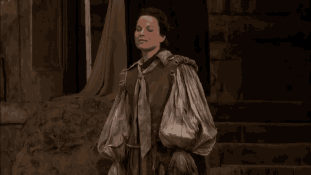 a woman in a costume stands in front of a stone wall