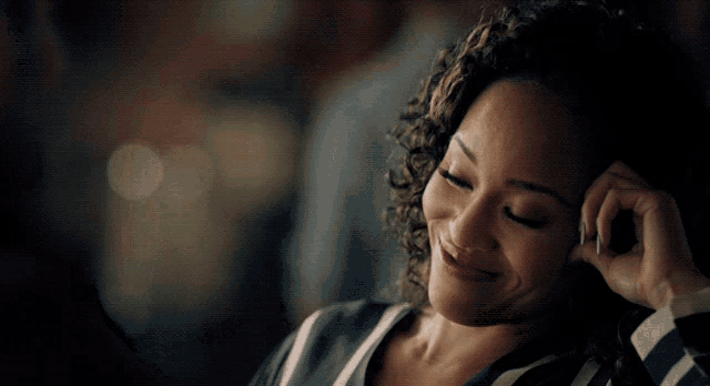 a woman with curly hair is smiling with her hand behind her ear