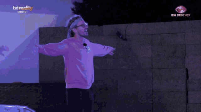a man in a pink sweater is standing in front of a big brother sign