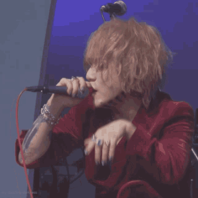 a man with blonde hair is singing into a microphone while wearing a red jacket