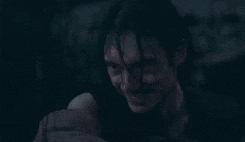 a man with blood on his face is holding a woman 's arm in the dark .