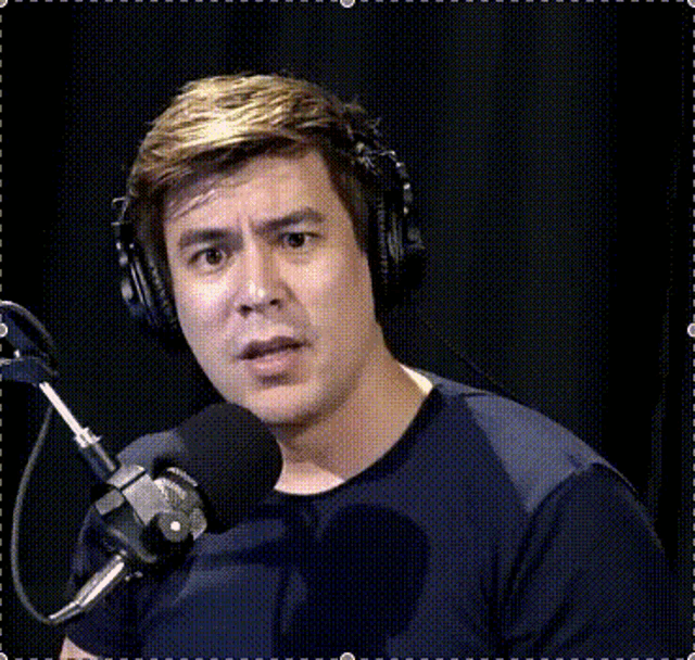a man wearing headphones and a black shirt is speaking into a microphone