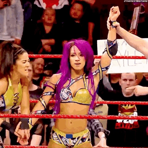 a woman with purple hair is standing in a wrestling ring holding her fist up .