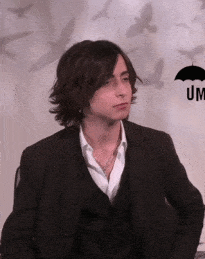 a man in a suit is sitting in front of an umbrella with birds behind him