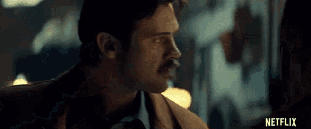 a man with a mustache is holding a gun in a dark room .