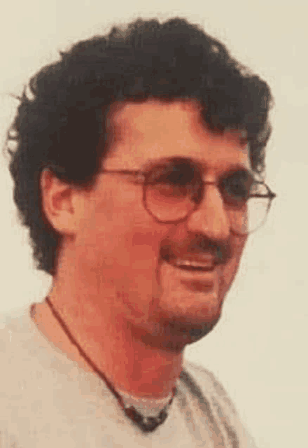 a man with curly hair and glasses is smiling and wearing a necklace .