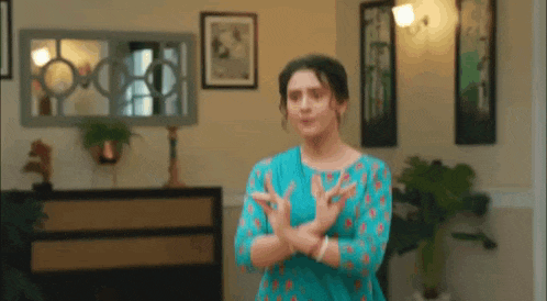 a woman in a blue shirt is standing in a living room with her hands crossed .