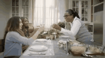 a group of women are sitting at a table toasting with wine .
