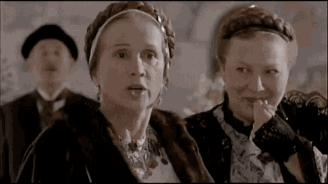 two women are sitting next to each other in a room with a man in a hat .