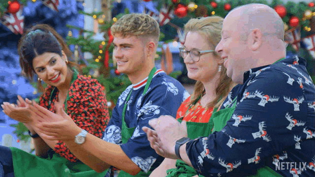 a group of people are clapping in front of a christmas tree and a netflix logo