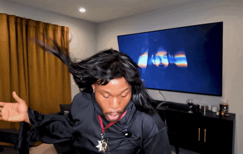 a man with long hair is dancing in front of a tv