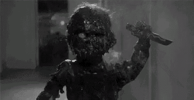 a black and white photo of a zombie holding a knife in a room .