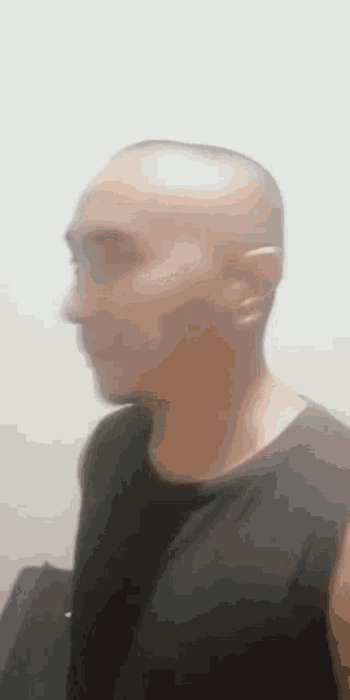 a man with a shaved head is wearing a black shirt and standing in front of a white wall .