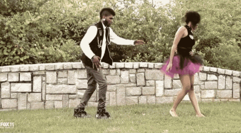 a man and a woman are dancing in front of a brick wall with fox 11 written on the bottom right