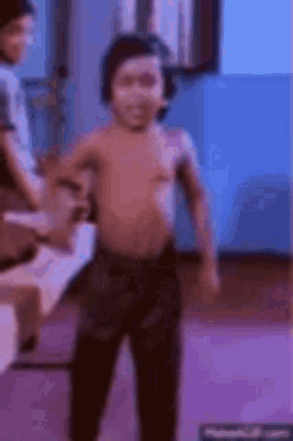 a young boy without a shirt is standing in a living room .