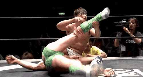 a man in green shorts is wrestling another man in white shorts in a ring .