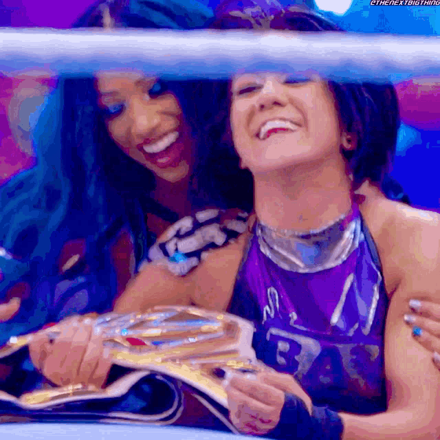 two women are posing for a picture in a wrestling ring and one is holding a championship belt