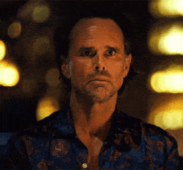 a man with a beard and a blue shirt is looking at the camera with a serious look on his face .