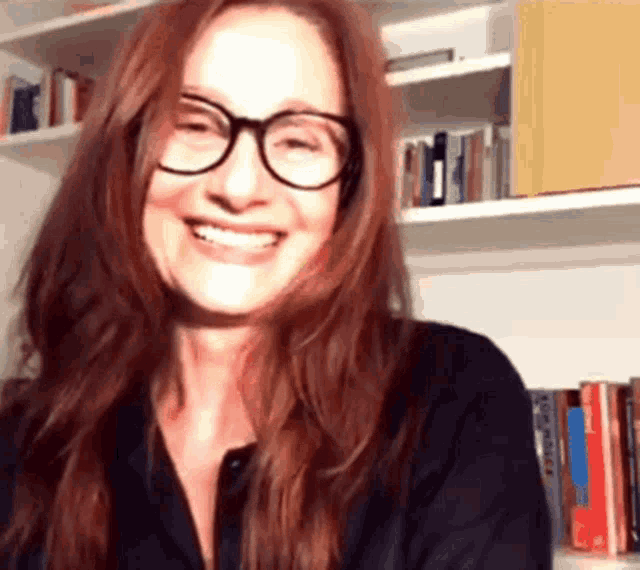 a woman with red hair wearing glasses and a black shirt smiles