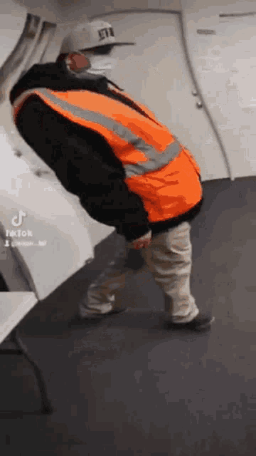 a man wearing a safety vest and a hat is walking on a carpet .