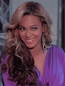 a woman wearing a purple top and earrings smiles