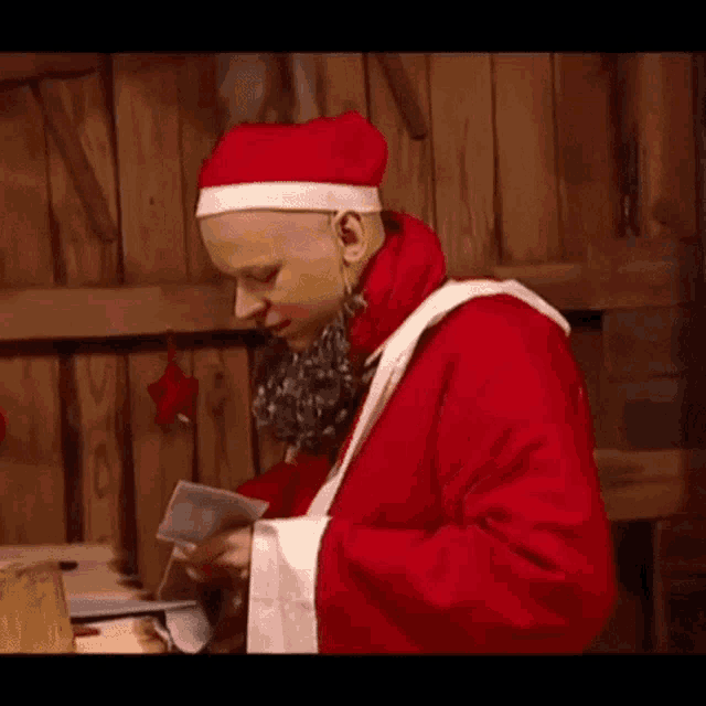a bald man dressed as santa claus is holding a piece of paper