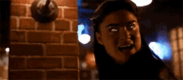 a woman is standing in front of a brick wall with her mouth open and making a funny face .