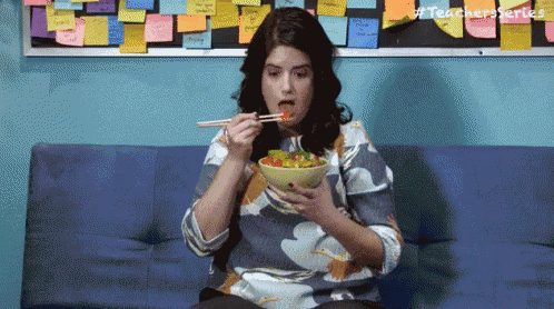 a woman is eating a salad with chopsticks on a couch .