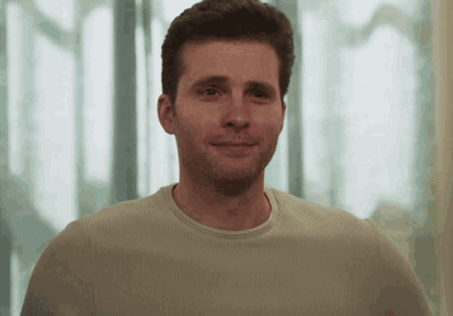 a man with a beard wearing a tan sweater smiles