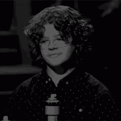 a young boy with curly hair is singing into a microphone .