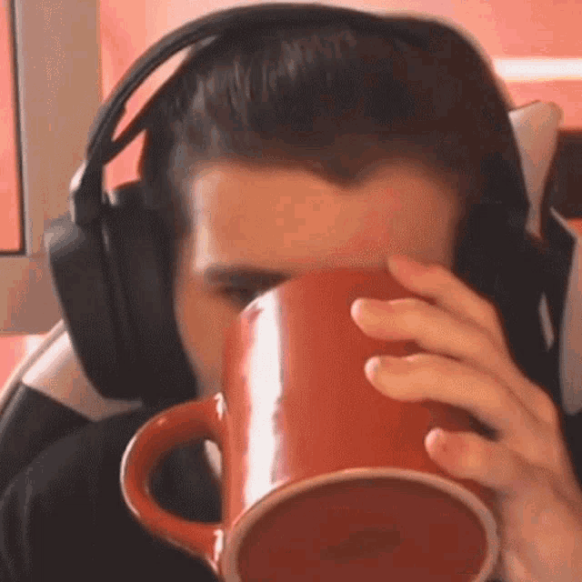 a man wearing headphones is drinking from a red coffee mug
