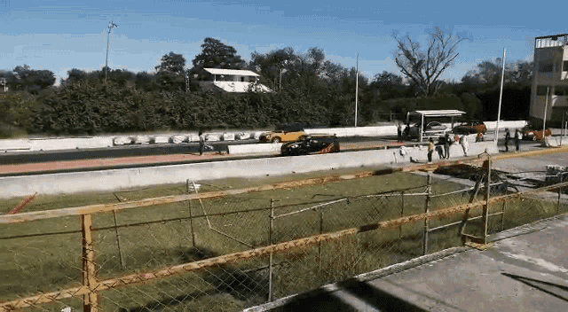 two cars are racing on a race track with a fence surrounding it