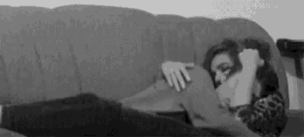 a woman is laying on a couch holding a pillow and covering her face .